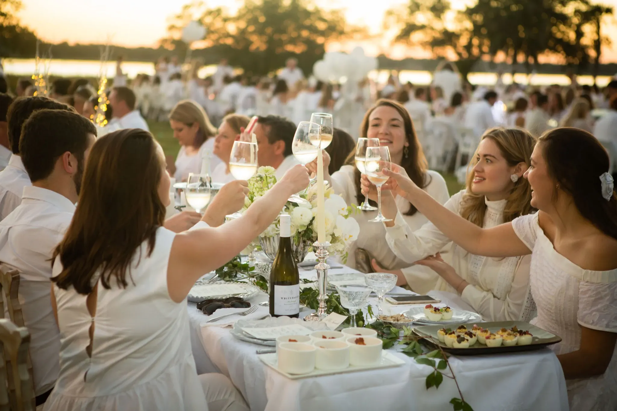 Guests in white raising glasses at a VIBE-staffed Soirée en Blanc event at sunset